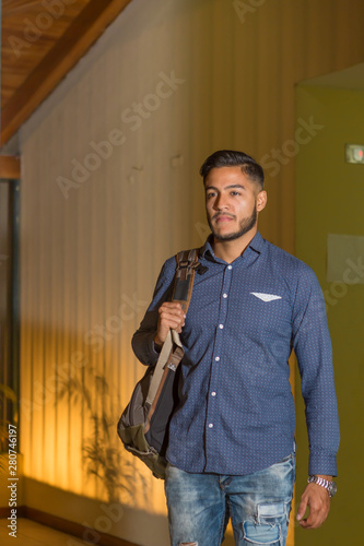 young man walks out of his home building with back pack to go to work and study.