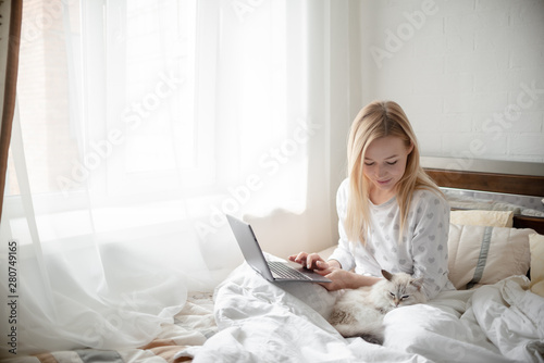 Blonde Giirl typing and using laptop hygge with fluffy cat, pajama and blanket. Hugge and lagom concept comfort and simple life . Horizontal copyspace