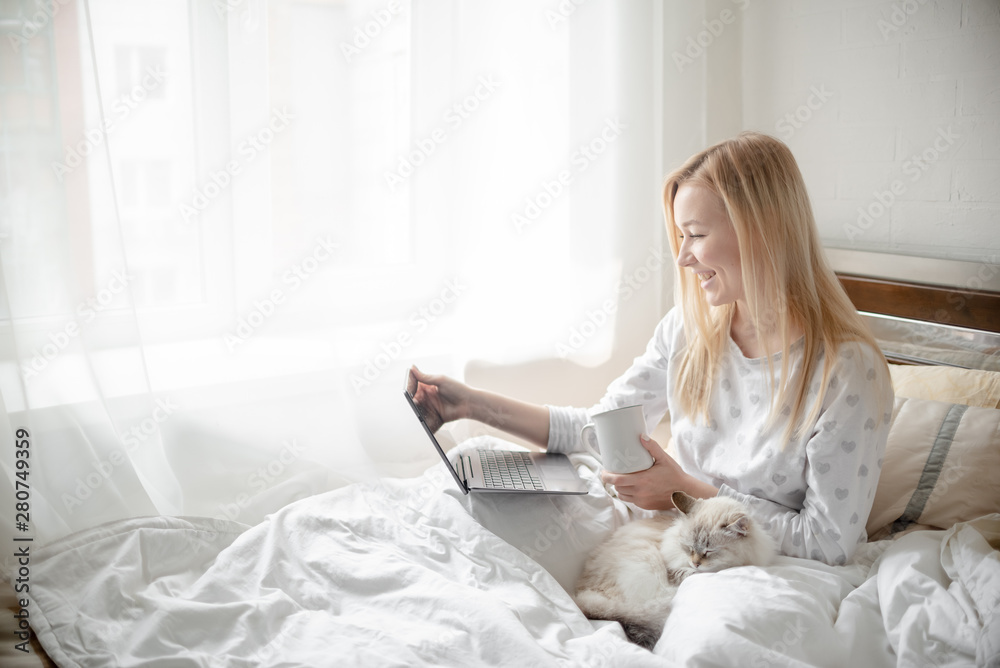Work from home concept . Blonde Giirl typing and using laptop. Hygge with fluffy cat, pajama and coffee cup. Horizontal copyspace Work from home concept . Blonde Giirl typing and using laptop. Hygge with fluffy cat, pajama and coffee cup. Horizontal copyspace