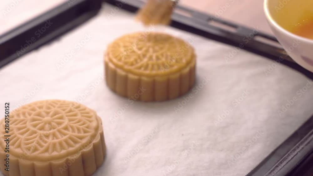 Woman smearing egg on cantonese moon cake pastry with brush befor baking on baking tray for traditional Mid-Autumn festival, close up. Woman smearing egg on cantonese moon cake pastry with brush befor baking on baking tray for traditional Mid-Autumn festival, close up.