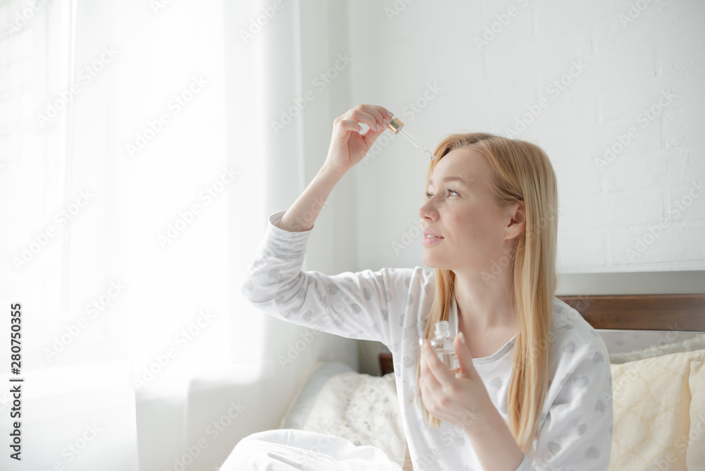 Young beautiful blond woman uses serum for face. The concept of facial skin care and aging. Horizontal copyspace Young beautiful blond woman uses serum for face. The concept of facial skin care and aging. Horizontal copyspace