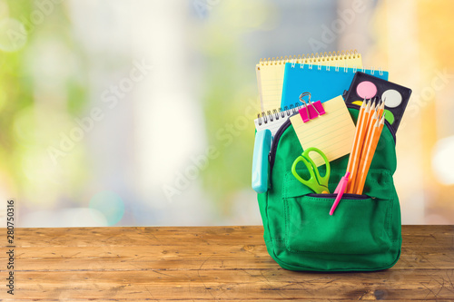 Back to school concept with bag backpack and school supplies on wooden table over abstract background