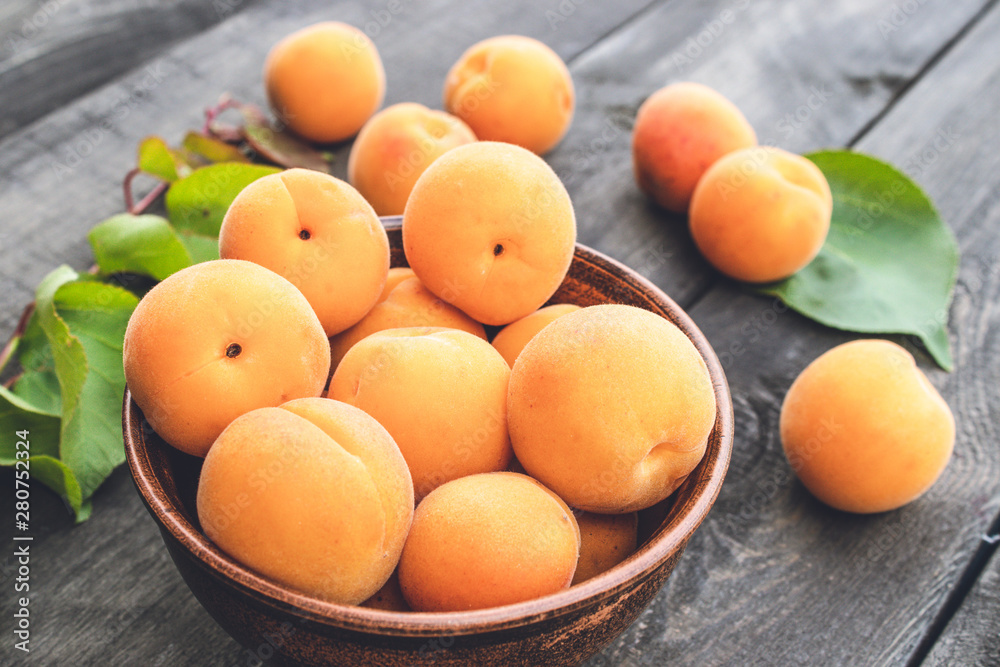Delicious ripe apricots in a bowl next to green leaves on a wooden table. Delicious ripe apricots in a bowl next to green leaves on a wooden table.