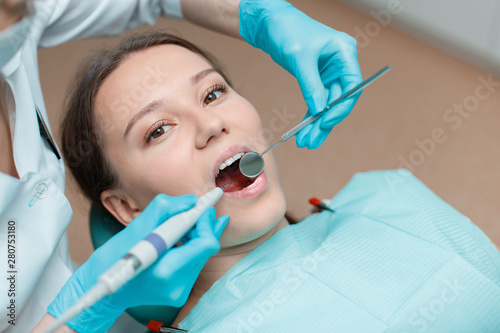 Fototapeta Naklejka Na Ścianę i Meble -  Patient in dental chair. Dentist's hands with blue gloves work with a dental tools. Beautiful young woman having dental treatment at dentist's office.