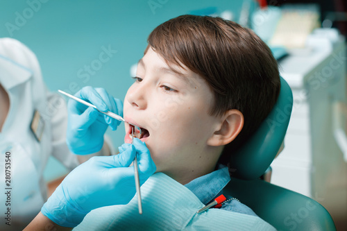 Little boy with open mouth examining dental inspection at dentist office. Dentist s hands with blue gloves work with a dental tools. Healthy teeth concept.