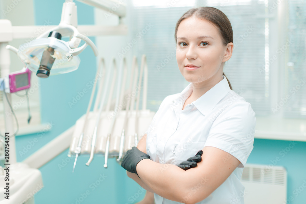 Portrait of beautiful female dentist with crossed arms in clinic. Young woman doctor standing in her office.