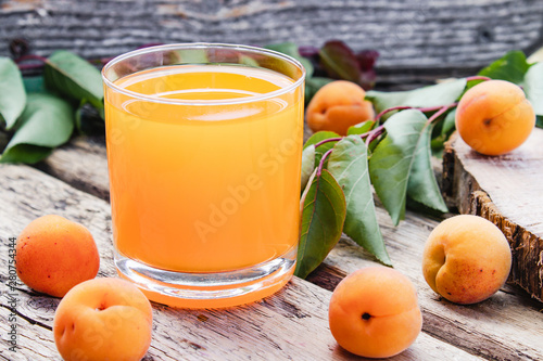 Fresh apricot juice with apricots and a branch with green leaves on the background of old boards.