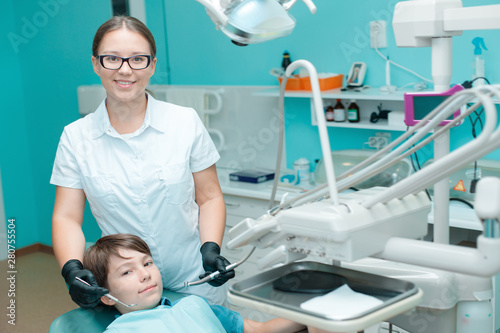 Patient in dental chair. Beautiful female dentist in black gloves work with a tooth drill and a mirror. Little boy having dental treatment at dentist's office.