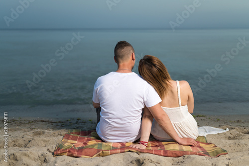 Romantic portrait of couple in love hugs sitting on the beach at the sunset. Against the backdrop of the sea.