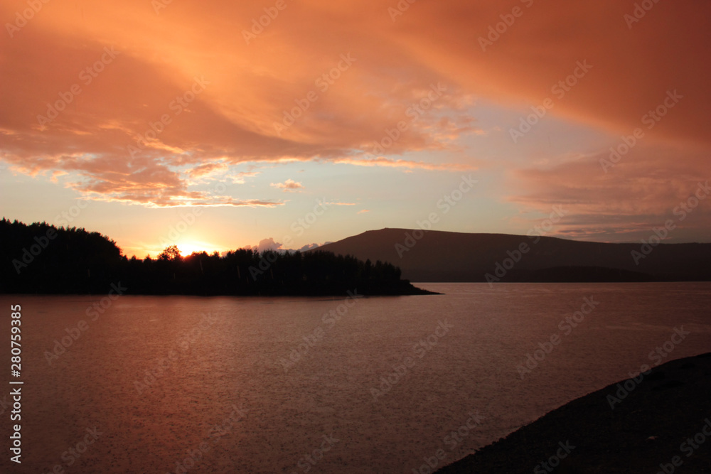 orange and pink clouds at sunset over a mountain lake