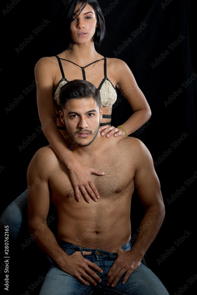 Couple poses standing up. He is sitting and she is standing behind him. They are young in theirs twenties, caucasian. They are looking at the camera. He is shirtless. Couple poses standing up. He is sitting and she is standing behind him. They are young in theirs twenties, caucasian. They are looking at the camera. He is shirtless.