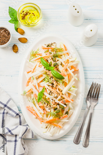 Turnip carrot apple salad with yogurt dressing, nuts, seeds on wooden background. Top view, space for text