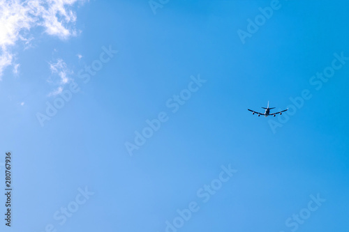 the silhouette of a flying plane in the blue sky and clouds on the background