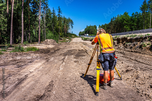 Surveyor engineer (worker) with equipment (theodolite or total positioning station) on the construction site of the road or highway