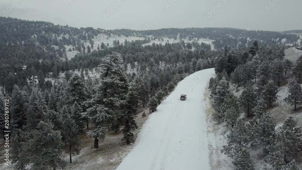 Cinematic Aerial of Lonely Isolated Car Driving on Snowy Countryside Road By Highway and Forest Under Winter Blizzard
