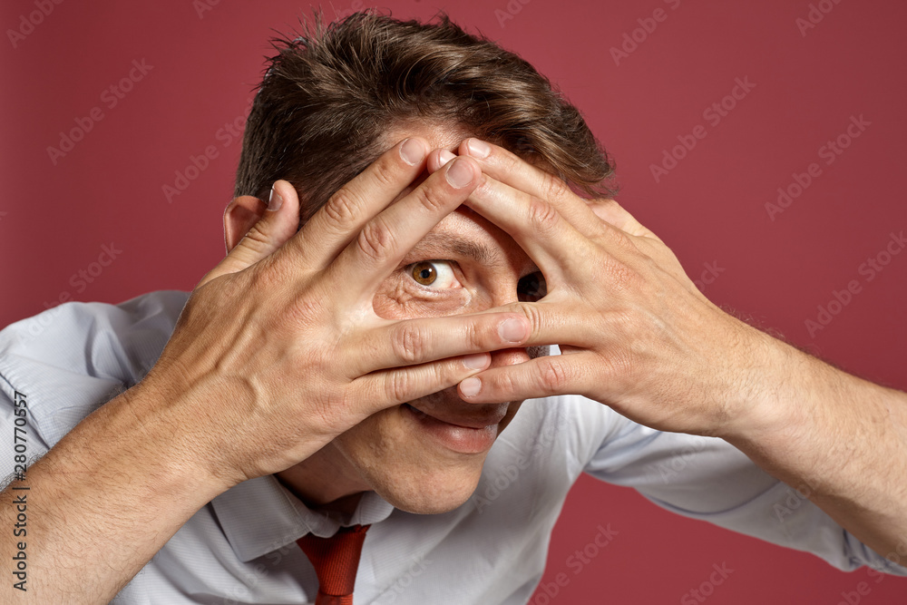 Portrait of a young brunet man posing in a studio against a red background.