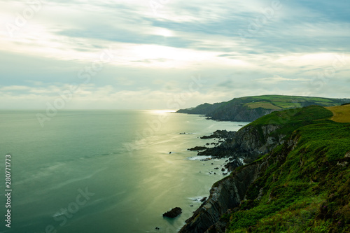 North Devon rock coast with cliffs and sharp lines during sunrise with sun reflection in the sea under cloudy sky