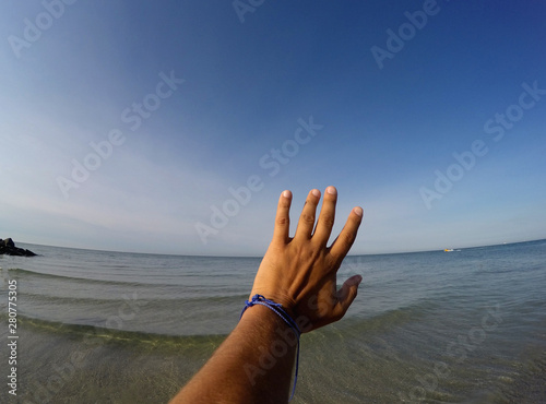the hand stretches to the blue sky against the background of the sea