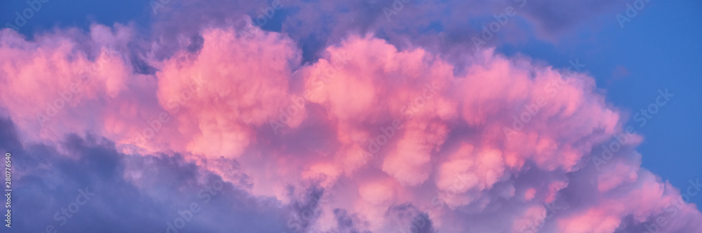 Colorful sky background with puffy clouds of pink and purple after summer rainstorm. Heaven at sunset