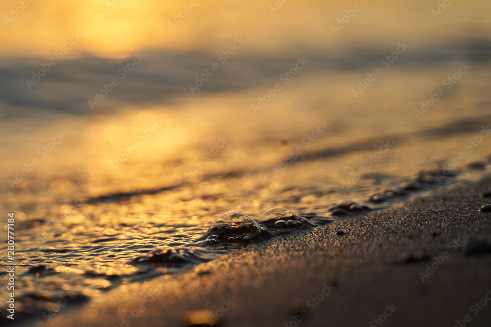Closeup of water bubble from the waves on the sandy coast at sunset. Golden hour background. Copy spase Closeup of water bubble from the waves on the sandy coast at sunset. Golden hour background. Copy spase