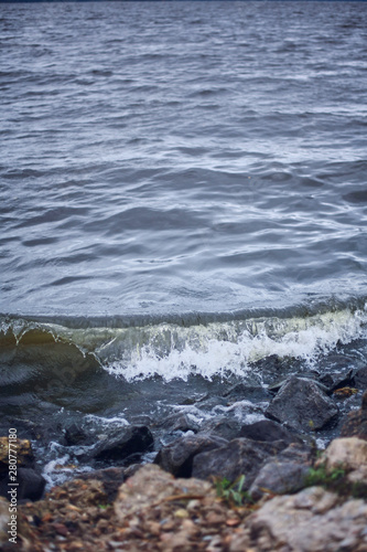 Small wave on the stone shore. Sea or lake with dark water. Wild Nature Dramatic Background
