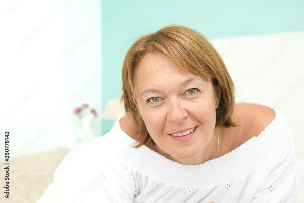 Happy woman lying face down and looking at the camera in the bedroom bed in a clear environment that corresponds to a Scandinavian concept called Lagom Happy woman lying face down and looking at the camera in the bedroom bed in a clear environment that corresponds to a Scandinavian concept called Lagom