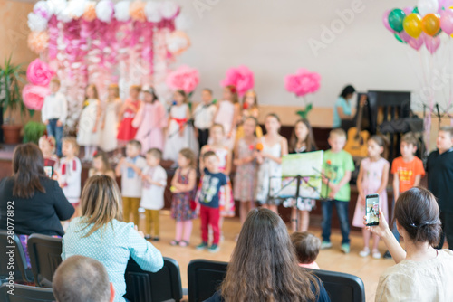 Children's party in primary school. Young children on stage in kindergarten appear in front parents. blurry