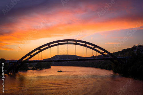 Colorful Pennybacker Bridge Sunset from over River with mountains in the background and a boat on the lake | texas landmark