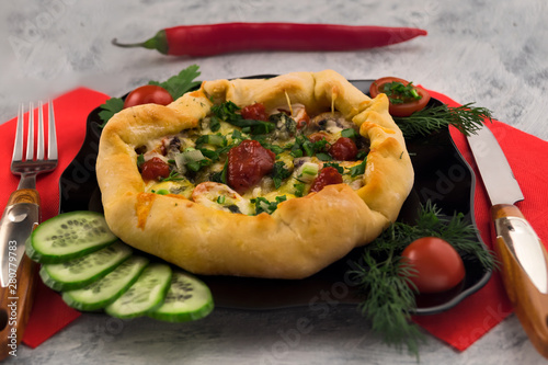 Hot tasty pizza with spicy sauce. Fresh vegetables with dill and parsley. Cutlery - fork and knife. Light background.