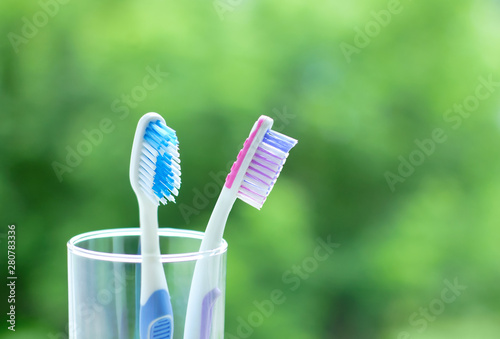 Two white plastic toothbrushes in a glass beaker. On a green blurred background.