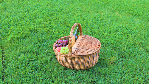 Wicker picnic basket with white and black grapes and wine on green grass outside