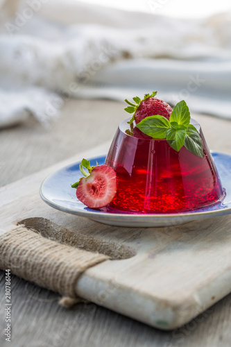 Photo of summer Jelly Dessert with strawberry. Garnished with a sprig of fresh basil on light background.