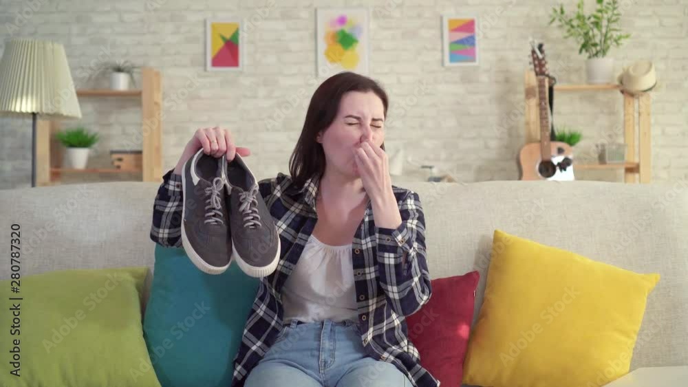Young woman holding shoes in her hands and smell unpleasant
