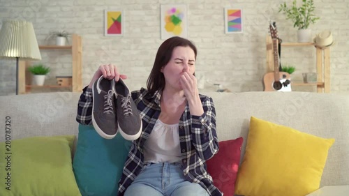 Young woman holding shoes in her hands and smell unpleasant