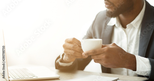 Pensive afro businessman drinking coffee at workplace