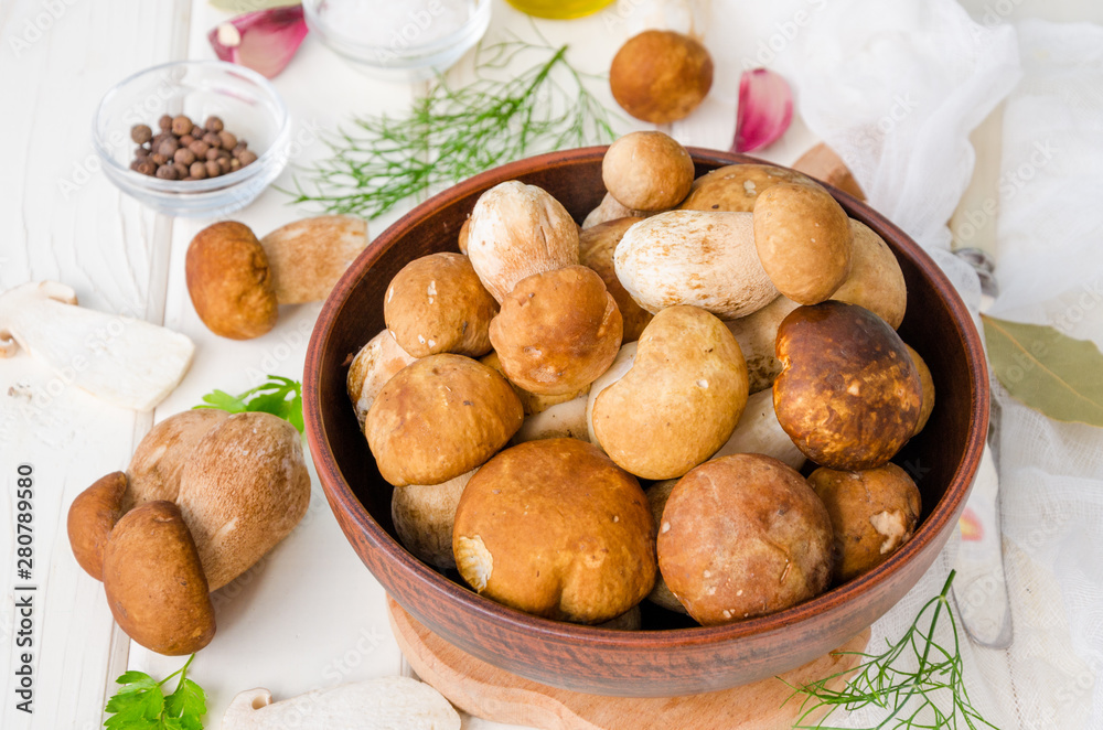 Fresh forest white mushrooms in a bowl with spices and fresh herbs on a wooden background