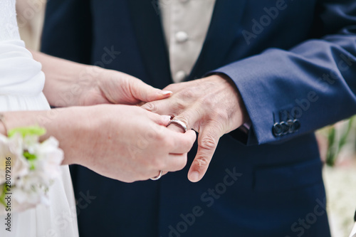 Close-up of the hand of the bride puts a wedding ring on the grooms finger, the ceremony on the street, selective focus
