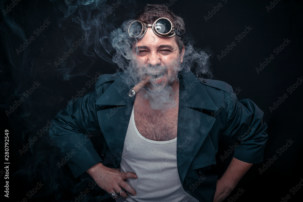 Grunge man, steampunk dressed, smoking a cuban cigar. Black studio background