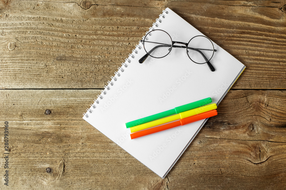 Green and yellow markers, a notebook and glasses on a wooden background. The concept of school, creativity, childhood. Green and yellow markers, a notebook and glasses on a wooden background. The concept of school, creativity, childhood.