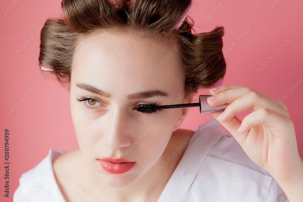 nice cheerful young the girl in the curler paints an eyebrow on pink background nice cheerful young the girl in the curler paints an eyebrow on pink background