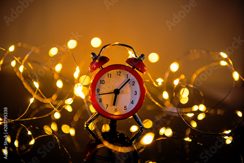 Alarm Clock And Christmas Lights Against Blurred Background. Winter Night photo