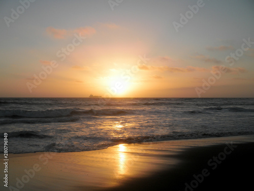 Sunset over Pacific ocean with large cargo ship in the background and waves rolling in on Ocean Beach