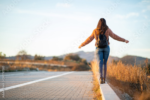 Beautiful woman walking and balancing on street curb or curbstone during sunset