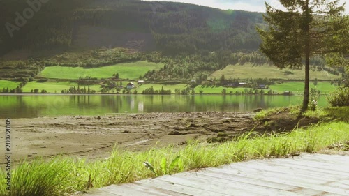 A rural panorama beach view of green farmland, trees, quiet lake and mountains in the countryside, nature summer scenery with sunlight in a perfect place for meditation, zen and recreation