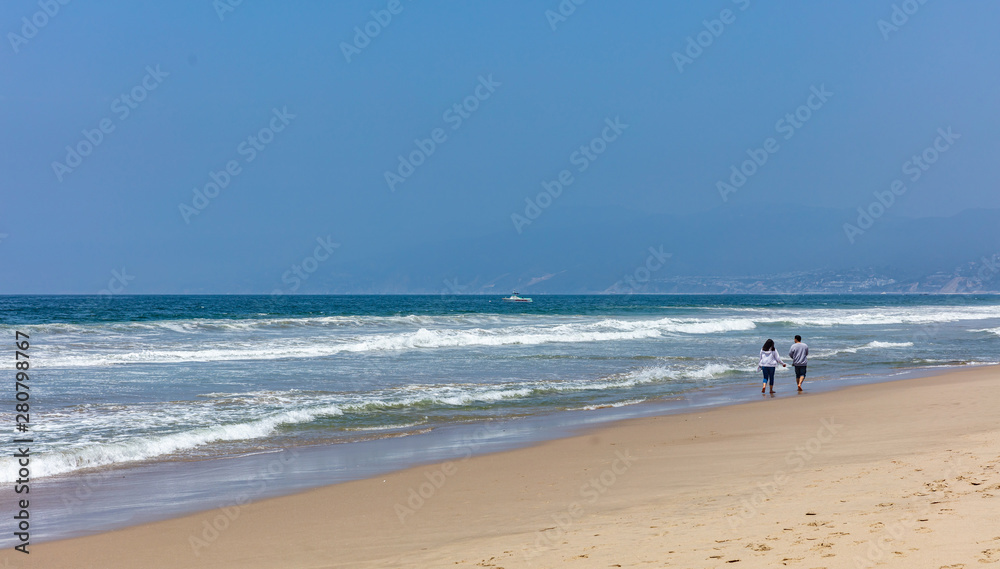 Young couple walking on the sandy beach. Blue ocean sea waves, clear blue sky in a sunny spring day