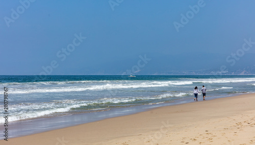 Young couple walking on the sandy beach. Blue ocean sea waves, clear blue sky in a sunny spring day