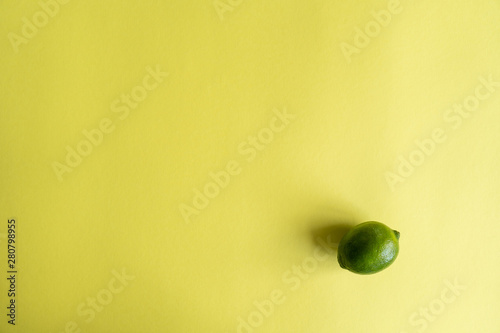 Fresh juicy green lime in the right-down corner of a yellow background. Top view