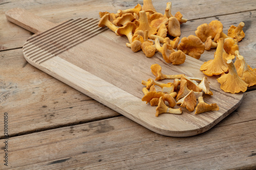 Fresh chanterelle mushrooms on wooden background with cutting board and copy space....