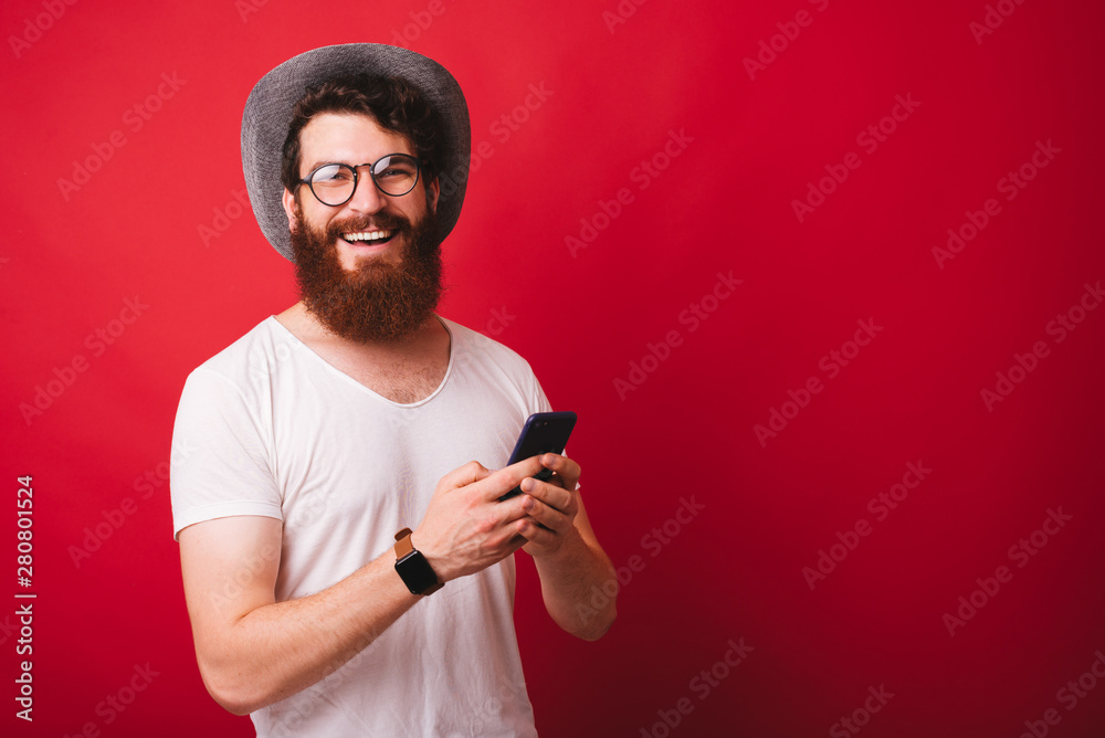 Photo of smiling young hipster man holding smartphone and looking at the camera Photo of smiling young hipster man holding smartphone and looking at the camera