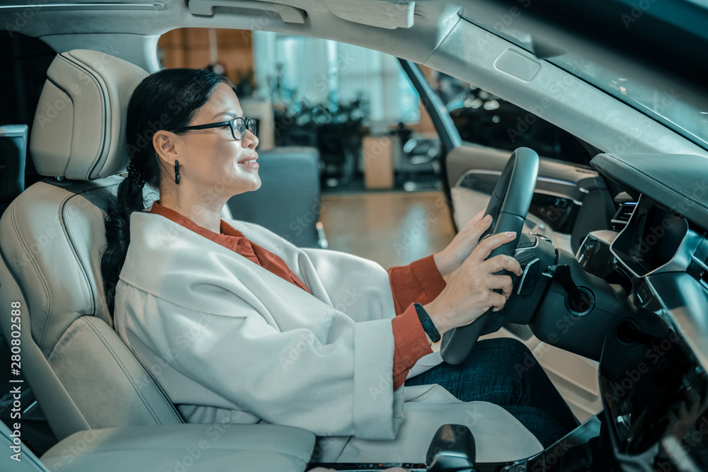 Woman sitting at the wheel in automobile showroom.